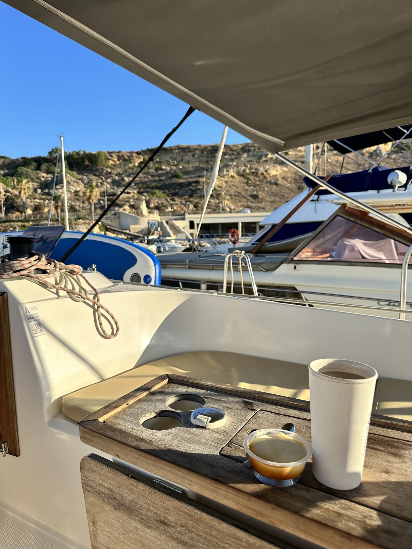 Cockpit table with coffee and marina boats nearby.